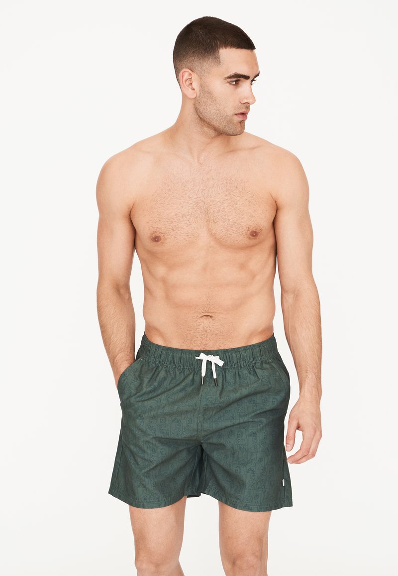 Vihreät kuviolliset uimapuvut, joissa on joustava vyötärö ja valkoinen nyöri. Materiaali vaikuttaa kevyeltä ja sopivalta vesikäyttöön.