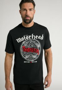 Sort bomulds t-shirt med "Mot�örhead" tekst og et "Ace of Spades" grafik i hvid og rød med detaljeret spar design. Korte ærmer.