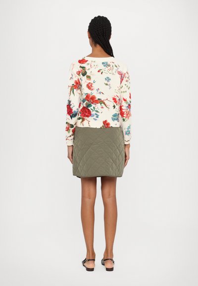 Pull en tricot à motif floral crème, mettant en avant des fleurs rouges et bleues. Associé à une jupe matelassée verte olive. Vue de dos, montrant les détails du design.