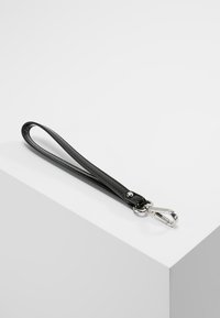 Bracelet de poignet en cuir noir avec clip métallique argenté posé sur une surface blanche inclinée.