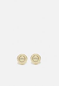 Pendientes de botón en tono dorado con diseño circular, que presentan un centro elevado y cinco pequeñas piedras transparentes. Nombre de la marca grabado alrededor del borde.
