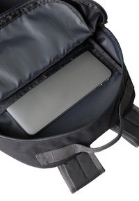 Mustast riidest sülearvutikott, millel on polsterdatud sisu. Sisemusest paistab hall sülearvuti, mille pind on sile, varustatud reguleeritavate rihmade ja lukuosaga.