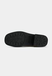 Semelle de chaussure en caoutchouc noir dotée d'un motif de bande de roulement avec des designs croisés et fléchés, offrant traction et stabilité sur diverses surfaces.