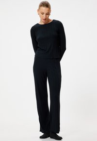 Zwart geribbeld loungepak met een lange mouw top en uitlopende broek met een subtiele gekartelde zoom. Zachte, lichte stof.