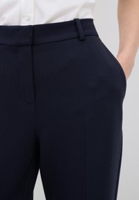 Pantaloni in blu navy con texture e vestibilità sartoriale, caratterizzati da una vita piatta e tasche laterali, realizzati in un tessuto leggero.