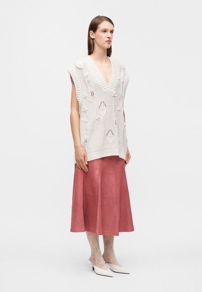 Gilet crème en maille avec motifs floraux et col en V, assorti à une jupe midi en cuir rose, des collants en dentelle, et des chaussures blanches à bout pointu.