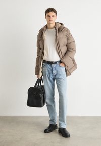 Casaco acolchoado xadrez castanho, camisa creme, jeans azul claro, mala preta e botas pretas. O casaco tem capuz e textura padrão.