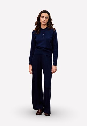 Ensemble en maille marine comprenant un pull à manches longues avec un col et des détails de boutons, associé à un pantalon large, texture lisse, coupe décontractée.