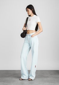 Λευκό κοντό μπλουζάκι με γραφικό τύπωμα, ανοιχτό μπλε φαρδιά τζιν, καφέ τσάντα ώμου, φορεμένο με ανοιχτούς σάνδαles.