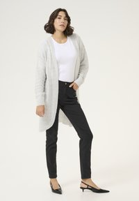 Svetlo siva pletena jakna z teksturiranim vzorcem, v kombinaciji s črnimi oprijetimi jeans hlačami in črnimi slingback petkami z ostro konico.