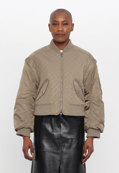 Giacca bomber trapuntata tagliata in beige tenue con chiusura a zip, polsini a coste e tasche laterali inclinate. Tessuto liscio e design imbottito.