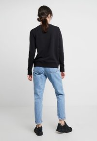 Felpa nera realizzata in un tessuto morbido, abbinata a jeans azzurri con orlo arrotolato. Sneakers nere completano l'outfit casual. Vista posteriore.