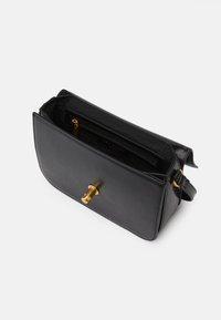 Mala de mão em couro preto com um design estruturado, apresentando um fecho de metal dourado e um bolso interior. A superfície tem uma textura lisa.