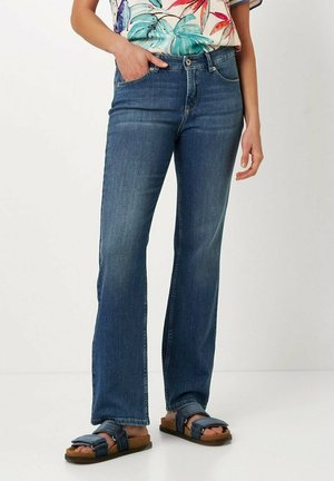 Blue denim flared jeans featuring a mid-rise waist, five-pocket design, and subtle whiskering, paired with brown sandals.