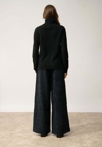 Schwarzer, hochgeschlossen Pullover kombiniert mit weit geschnittenen, strukturierten navy Cordhose. Das Ensemble zeichnet sich durch klare Linien und eine lockere Passform aus.