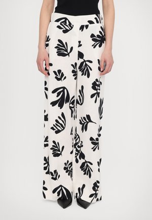 Wide-leg pants in a white fabric with a black botanical print. Features a smooth waistband and is worn with pointed black shoes.