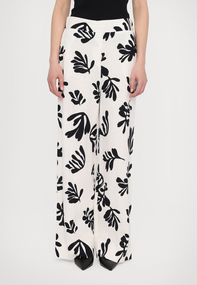 Wide-leg pants in a white fabric with a black botanical print. Features a smooth waistband and is worn with pointed black shoes.