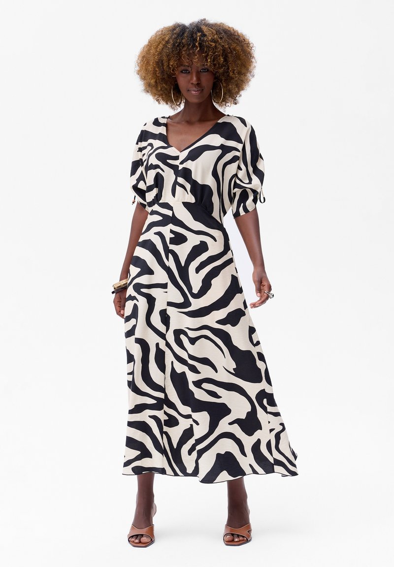 Schwarz- und cremefarbenes Zebra-Muster-Maxikleid mit kurzen Puffärmeln und V-Ausschnitt. Glatter Stoff, fließende Form und seitliche Schlitze.