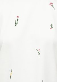 Λευκό ύφασμα με διασκορπισμένα μικρά κεντημένα λουλούδια σε ροζ, κίτρινο και πράσινους μίσχους, τοποθετημένα ανομοιόμορφα στην επιφάνεια.