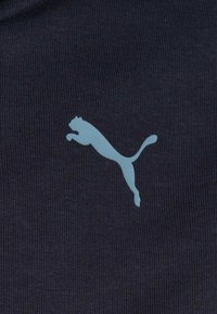 Logo di puma che salta in azzurro chiaro su uno sfondo di tessuto lavorato a maglia blu scuro.