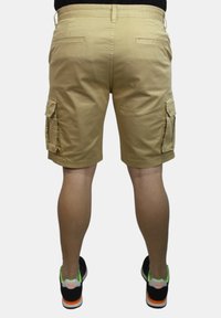 Pantaloni cargo color khaki con tasche laterali, progettati in una vestibilità rilassata. Il tessuto è morbido e presenta un elastico in vita e dettagli di cucitura.