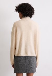 Maglione beige oversize con una texture morbida, collo alto e spalle scese, abbinato a una mini gonna grigia scura e strutturata.