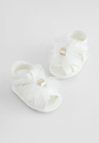 White baby sandals feature soft fabric, open toes, layered tulle accents, and a gold-tone buckle. Velcro strap ensures secure fit.