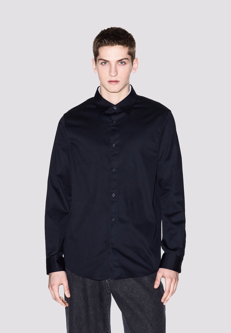Camicia blu navy con colletto, maniche lunghe e dettagli ricamati sul fronte. Tessuto liscio con una finitura lucida.