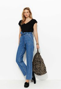 Haut noir à manches courtes, jean en denim bleu taille haute avec une ceinture à nouer, chaussures noires et sac à imprimé léopard. Fond blanc.
