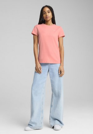 Roze ribgebreide T-shirt met korte mouwen, gecombineerd met lichtblauwe wijdvallende jeans en witte sneakers. Heeft een klein logo op de borst.