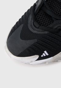 Černá sportovní obuv s horní částí z mřížky, texturovanými detaily, průhlednou gumovou podrážkou a vyšitým bílým logem na boku.