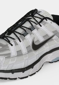 Nærbillede af en hvid og grå Nike løbesko med sorte snørebånd og et sort Swoosh-logo på siden.