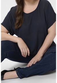 Haut à manches courtes bleu marine avec un décolleté en scoop, fabriqué en tissu léger et texturé, associé à un jean en denim foncé et des ballerines noires.