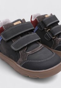 Zapatillas negras y marrones que presentan una mezcla de materiales de ante y textil, dos correas de Velcro, una suela de goma y acentos azules en contraste.