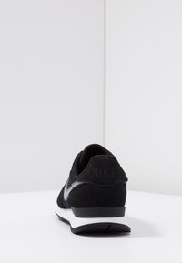 Black suede and mesh sneaker with a white midsole, featuring a gray swoosh logo and embossed branding on the heel. Rear view.