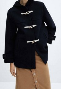 Cappotto di lana navy con cappuccio, dotato di chiusure a fibbia, due tasche anteriori e polsini larghi. Il tessuto ha una texture liscia e una struttura definita.
