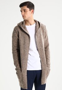 Cárdigan largo de frente abierto hecho de tejido de punto texturizado en tonos marrón y beige. Cuenta con capucha, bolsillos laterales y detalles acanalados en los puños y el cuello.