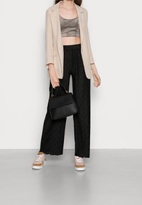 Beżowa blazer w kratkę na szarym crop topie, czarne szerokie spodnie o teksturowanej fakturze, czarna torba oraz różowe sneakersy z beżowymi akcentami.