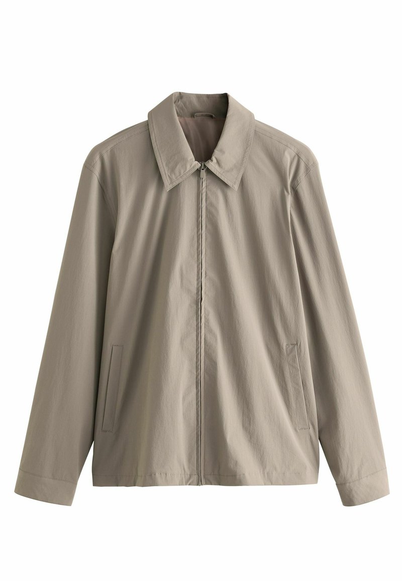 Chaqueta beige clara con un collar estructurado, cremallera frontal y bolsillos laterales. Hecha de una tela suave y ligera con costuras mínimas.