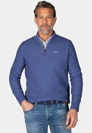 Blauwe rits-sweater van textuurstof, met staande kraag en ribgebreide mouwen. Draagt over een hemd met kraag, gecombineerd met spijkerbroek.