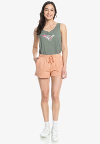 Groene tanktop met een hartafbeelding en roze ontwerpen, gecombineerd met perzikkleurige shorts met een elastische tailleband en zijzakken. Witte sneakers.