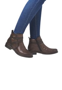 Bottines en cuir marron avec un bout arrondi, fermeture éclair sur le côté et deux sangles décoratives avec un anneau métallique sur le côté extérieur.