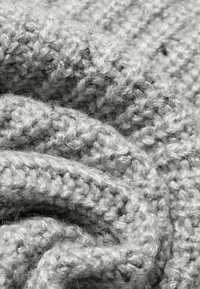 Gros plan d’un fil de laine gris doux et épais, tricoté dans un motif texturé avec des boucles et fibres visibles.