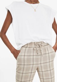 Chemise blanche à manches courtes avec une coupe décontractée, assortie à un pantalon à carreaux beige doté d'une taille élastique et d'un cordon de serrage.