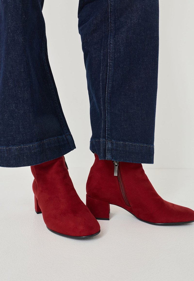 Botine negre din suede cu toc pătrat și fermoar lateral, asortate cu blugi evazați bleu închis, subliniind textura și contrastul de culori.