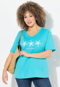 T-shirt turchese a maniche corte con scollo a V e grafica di stella marina, con la scritta "Ho bisogno di vitamina mare" in un carattere a contrasto.