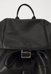 Sac à dos en cuir noir avec une finition texturée, un rabat repliable et une fermeture à boucle en métal argenté avec un accent logo.