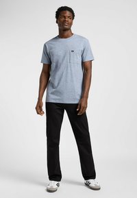 T-shirt da uomo a maniche corte, in azzurro melange, con taschino sul petto, abbinato a pantaloni neri e scarpe sportive bianche. Design forte e semplice.