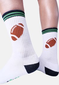 Calcetines blancos con un diseño de balón de fútbol marrón, puño a rayas verdes y negras, y acanalado texturizado. Detalles en el talón y la punta en negro.