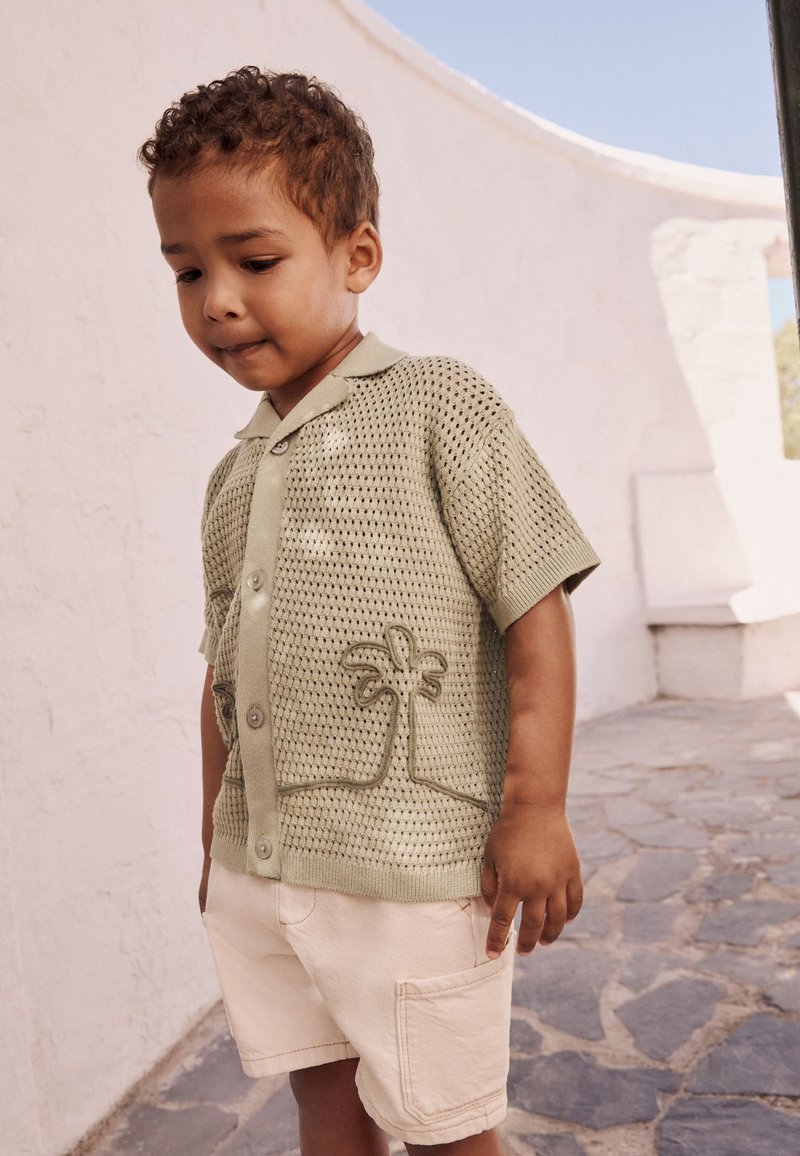 Light green mesh short-sleeve shirt with a palm tree design and buttons, paired with cream shorts featuring a side pocket.